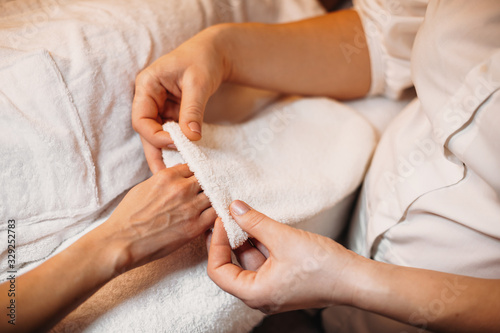 Caucasian spa professional is applying a special glove on the client's hand during a skin care procedure