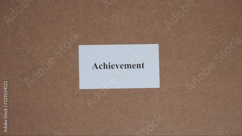 ACHIEVEMENT. Top shot - Hand puts paper card with word. CORE VALUE concept.
