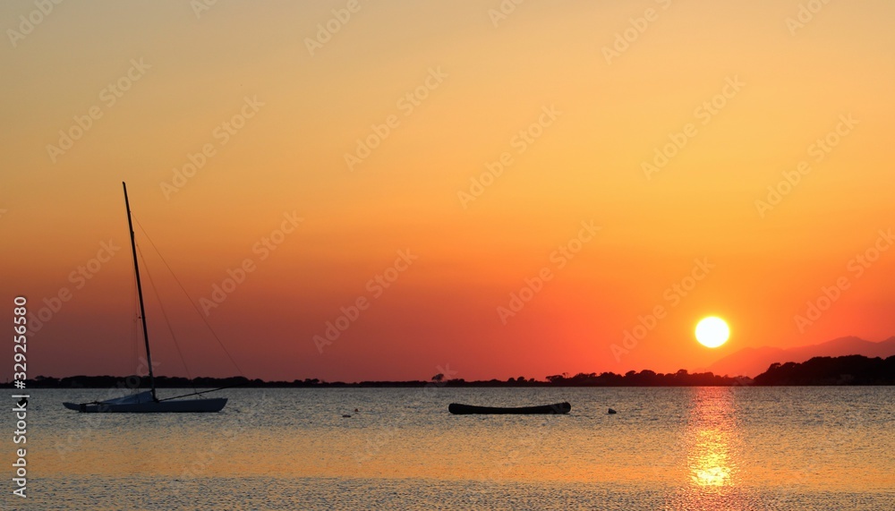 canoe and sailboat moored at sunset with headland in the background canoe and sailboat moored at sunset with headland in the background