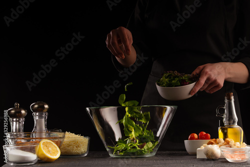 Chef cooks a salad with spinach leaves, freezing in motion. On a black background, healthy and wholesome food. Cooking, on a black background with space