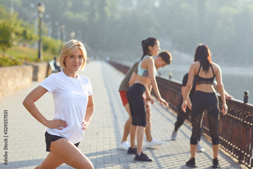 Obraz premium Sporty girl smiles on the background of friends athletes in the park