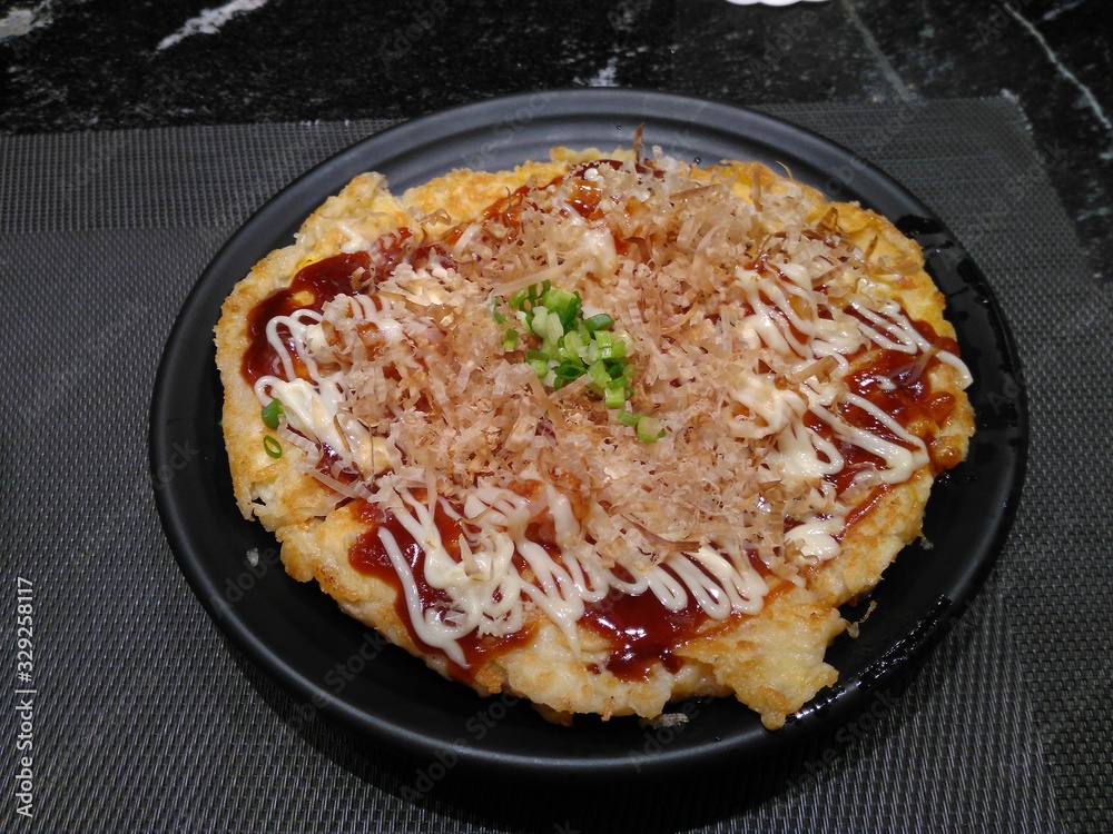 Japanese pizza on a dark plate on a black table Japanese pizza on a dark plate on a black table