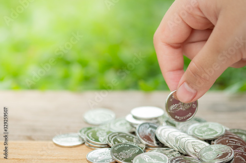 Money, Financial,Saving, Business loan concept, Closeup of women hand put coin to pile of silver coins on blurred nature background and copy space for text.