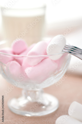 marshmallows in a glass bowl stands on a light table with a fork and milk. © Alek Smit