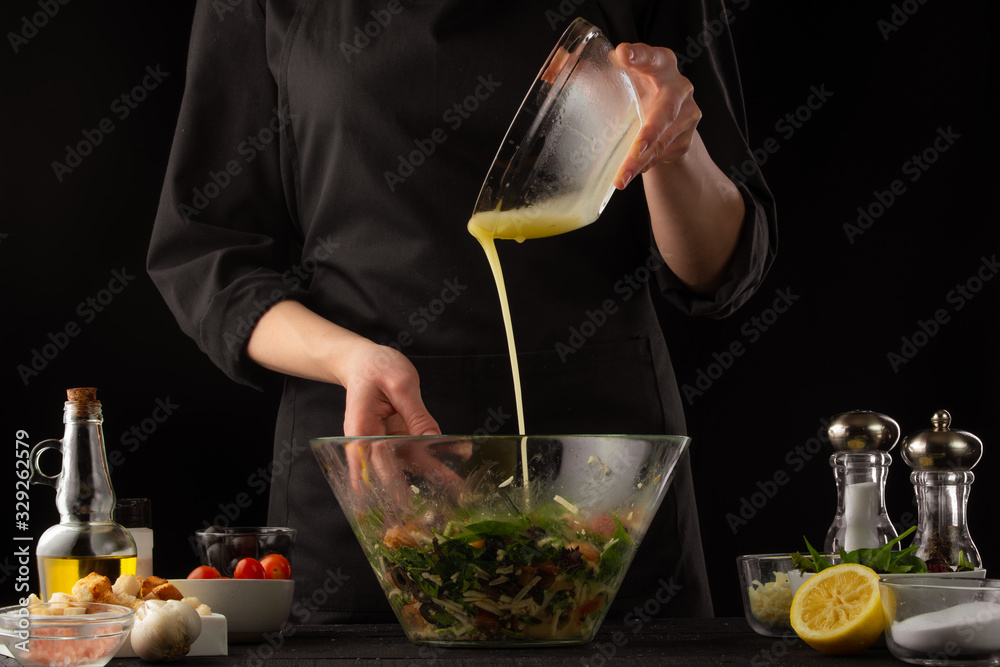Chef cooks a salad, pouring sauce on a black background. Cooking and home recipes. Chef cooks a salad, pouring sauce on a black background. Cooking and home recipes.