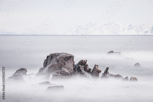 Sea ringed by snowy rocks and distant mountains. Lofoten, Norway.