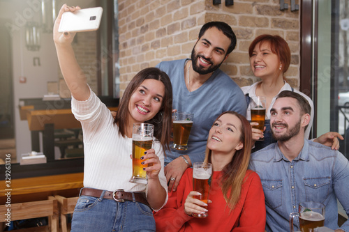 Group of friends taking selfies at beer pub. Young people enjoying celebrating together at the bar, using smart phone for taking photos
