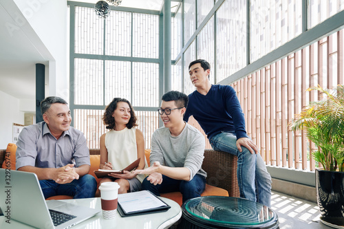 Cheerful multi-ethnic business team meeting in office lounge area and discussing project details