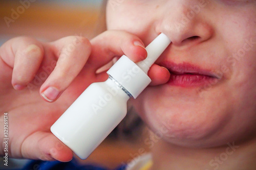 Little girl with bad cold and runny noseusing nasal spray. Defocused, blurred