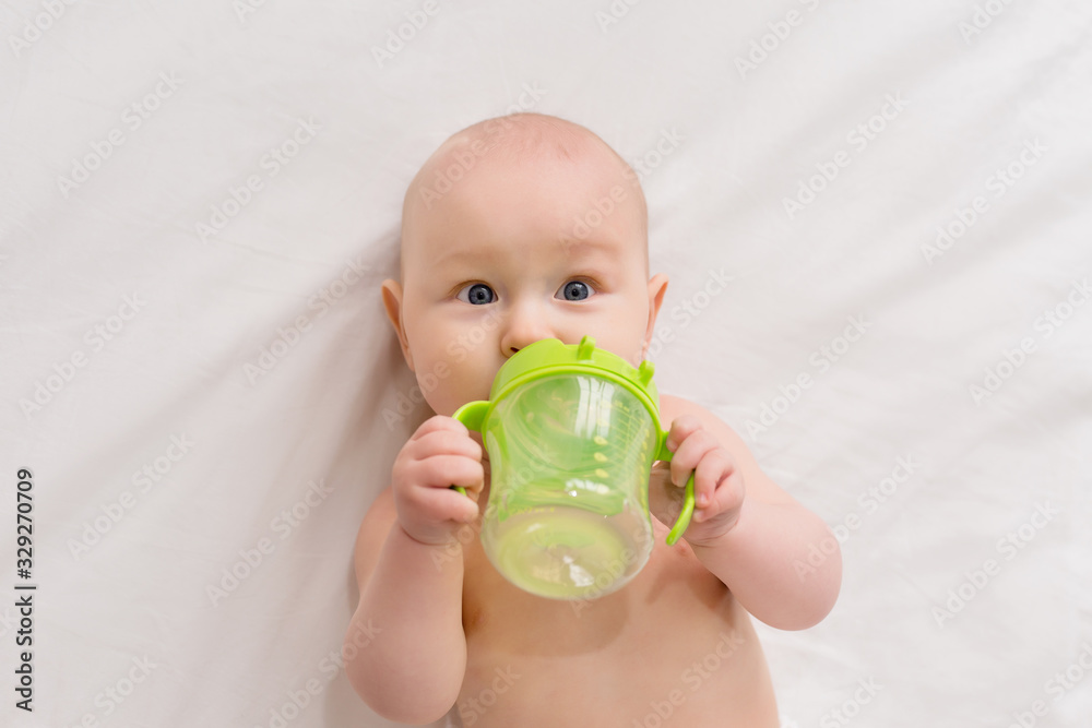 Baby boy drinks water from bottle lying on bed. Baby boy drinks water from bottle lying on bed.