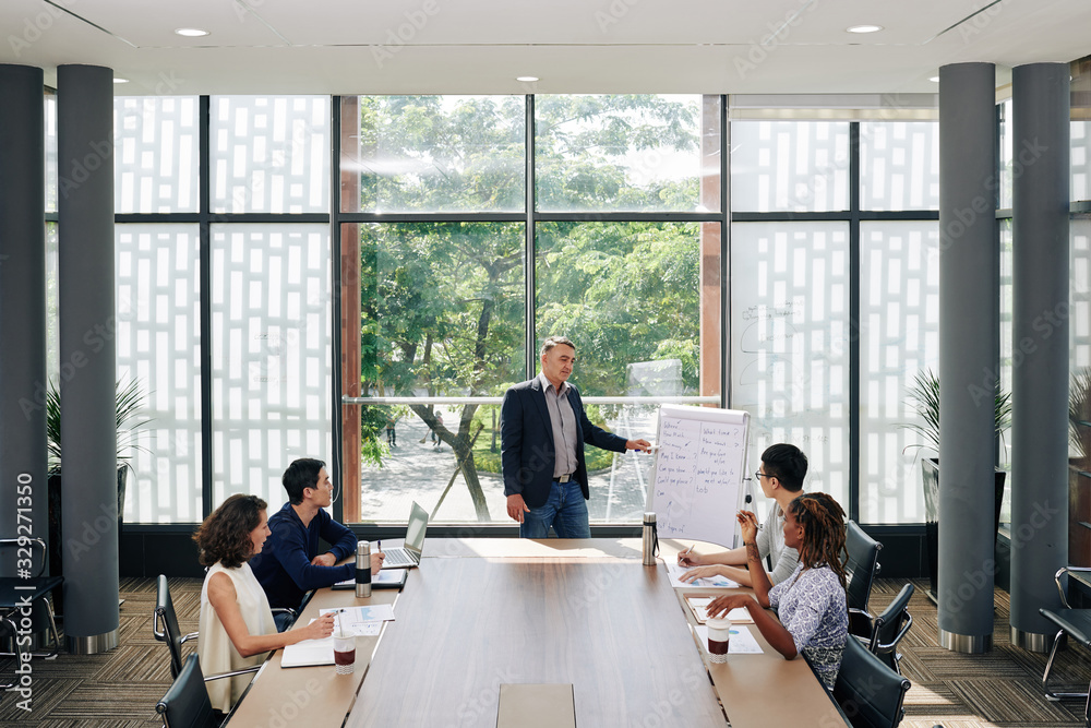 Fototapeta premium Mature entrepreneur talking to employees at meeting and explaining new marketing strategy