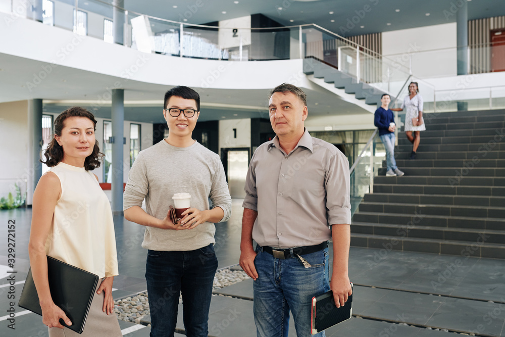 Obraz premium Multi-ethnic smiling successful business team standing in office hall and looking at camera