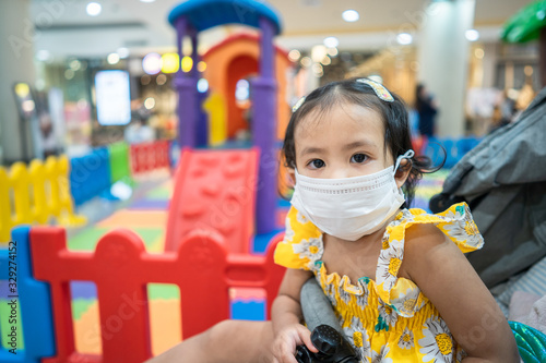 Little girl wearing medical face mask at playground in shopping mall to preventing flu, pollution and convid 19. photo