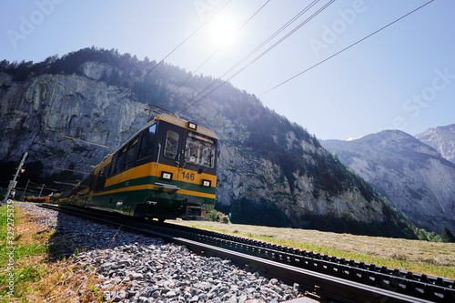 Beautiful mountains landscape. Yellow-green train running through the Swiss Grindelwald Village, Switzerland.