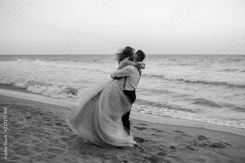Bride and groom having fun on sand beach near the sea. Beach wedding concept. The groom holding bride in his arms. Love kissing. Black and white. Copy space.