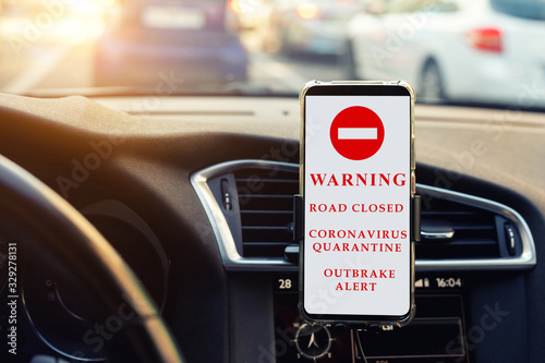 Modern smartphone device gadget mounted phone holder at car dashboard. showing traffic information message temporary road closed sign.Coronavirus outbrake quarantine alert info. Pandemia prevention photo