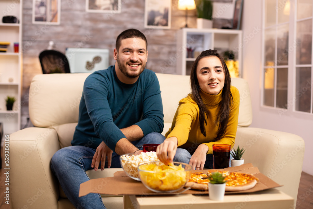 Beautiful young couple watching TV and eating fast food takeaway