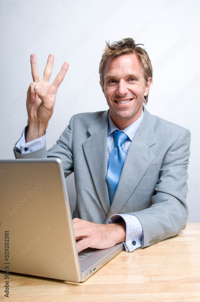 Smiling businessman sitting in front of his laptop computer holding up three fingers Smiling businessman sitting in front of his laptop computer holding up three fingers