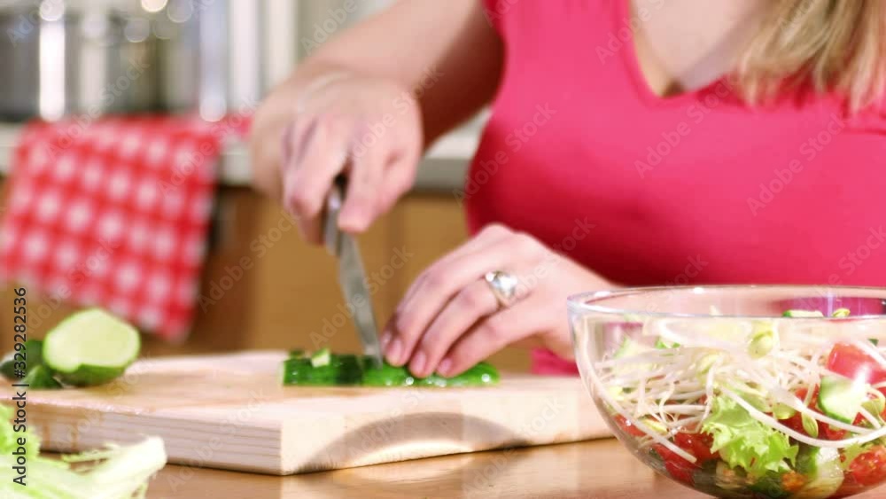 Hands of a young woman cuts a cucumber for a vegetable salad sitting at a table in the kitchen