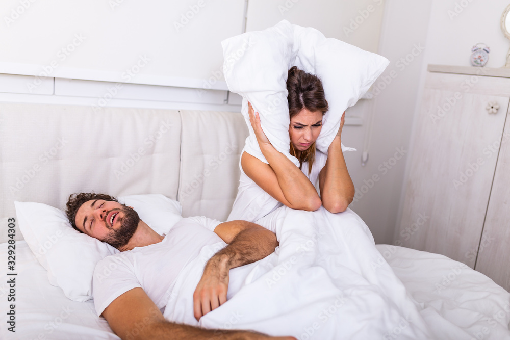 Snoring man. Couple in bed, man snoring and woman can not sleep. Picture of angry woman in bed with snoring man. Portrait of woman blocking ears with pillow while man snoring on bed Snoring man. Couple in bed, man snoring and woman can not sleep. Picture of angry woman in bed with snoring man. Portrait of woman blocking ears with pillow while man snoring on bed