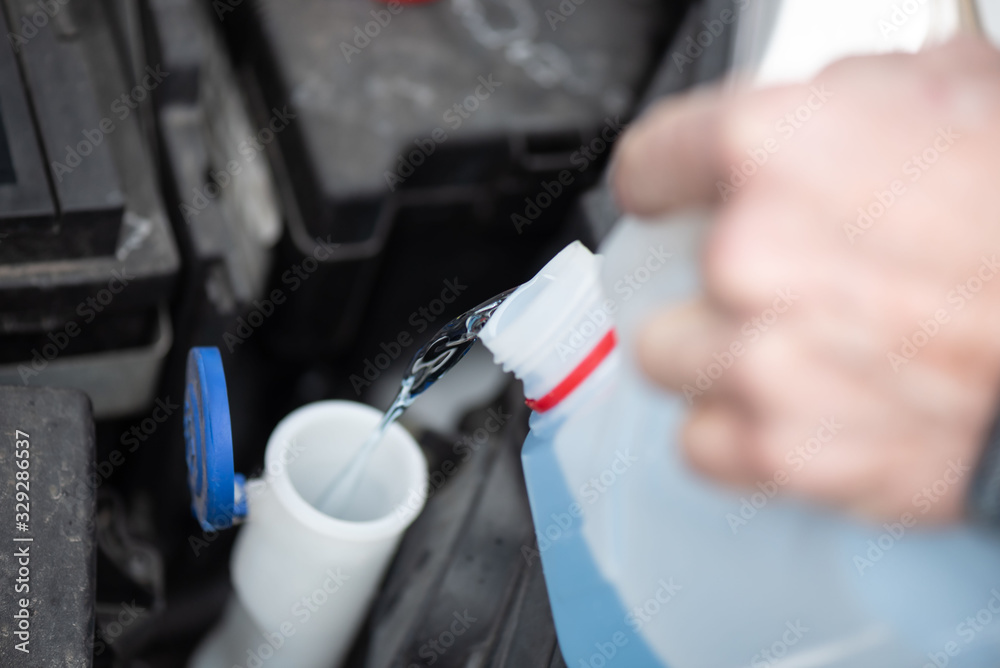 Hands of mechanic pouring windshield washer fluid in a car