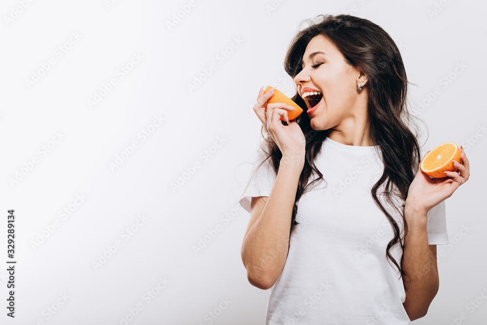 Playful cute brunette girl playing fool with halves of orange isolated white background copyspace Playful cute brunette girl playing fool with halves of orange isolated white background copyspace