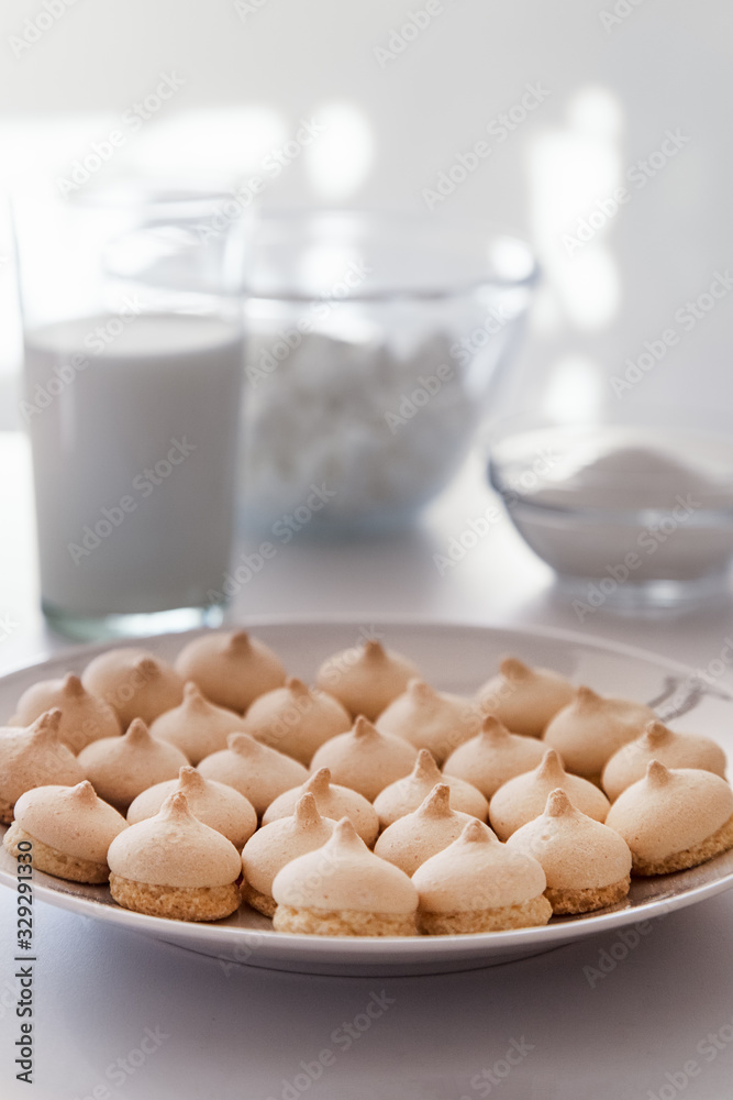 Merinque cookies in white plate. Glass of milk, white bowls background.High key food photography.
