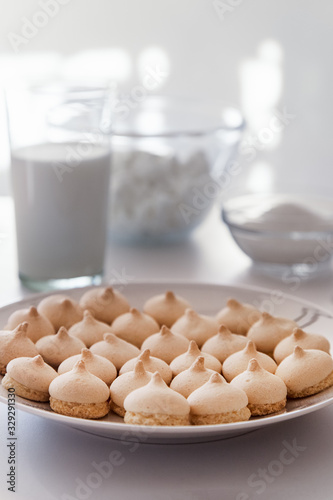 Obraz na płótnie Merinque cookies in white plate. Glass of milk, white bowls background.High key food photography. w salonie