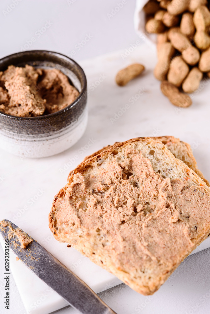Homemade peanut paste or butter in a bowl and bread and peanuts on white marble tray. Healthy nutrition. Selective focus Homemade peanut paste or butter in a bowl and bread and peanuts on white marble tray. Healthy nutrition. Selective focus
