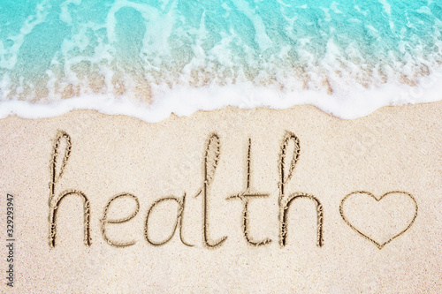 Health text and heart symbol written in sand. Ocean blue wave on background. Healthcare and wellness concept photo.