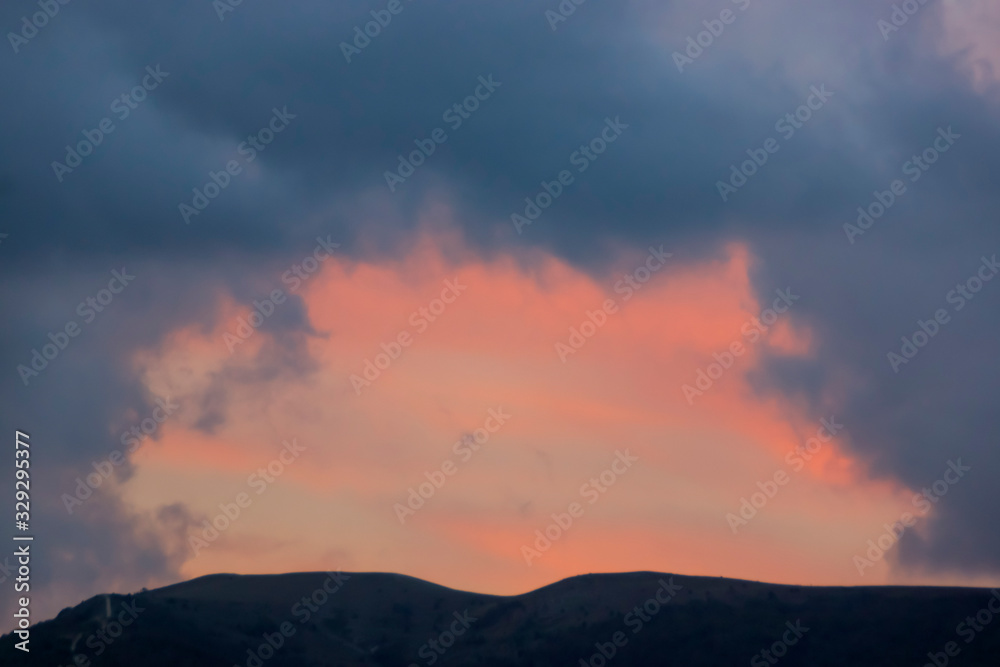 Play of color above the mountain in pink and blue clouds after sunset