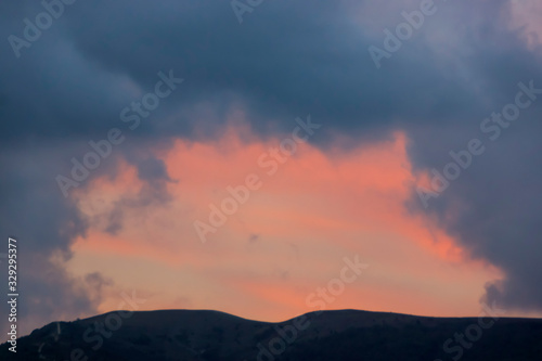 Play of color above the mountain in pink and blue clouds after sunset