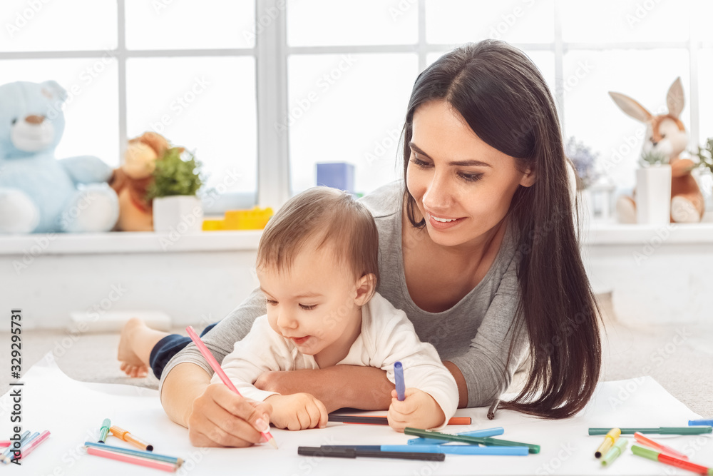 Motherhood. Mother and son lying on floor drawing together with color markers smiling concentrated close-up Motherhood. Mother and son lying on floor drawing together with color markers smiling concentrated close-up