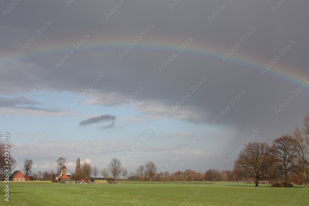 Naklejka premium Regenbogen, dunkle Wolken, Bauernhof, Bäume und Himmel