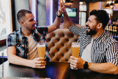 Photography Handsome cheerful friends giving high five while drink beer in pub