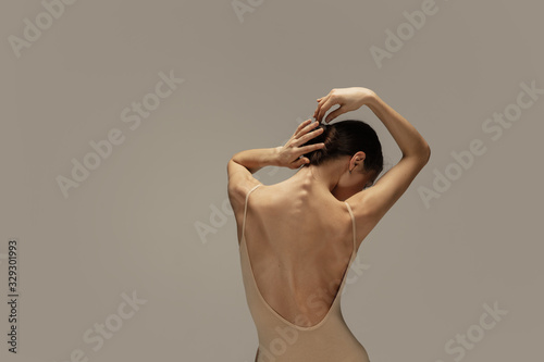 Graceful classic ballerina dancing, posing isolated on pastel brown studio background. Females back and hands. The grace, artist, movement, action and motion concept. Looks weightless, flexible.