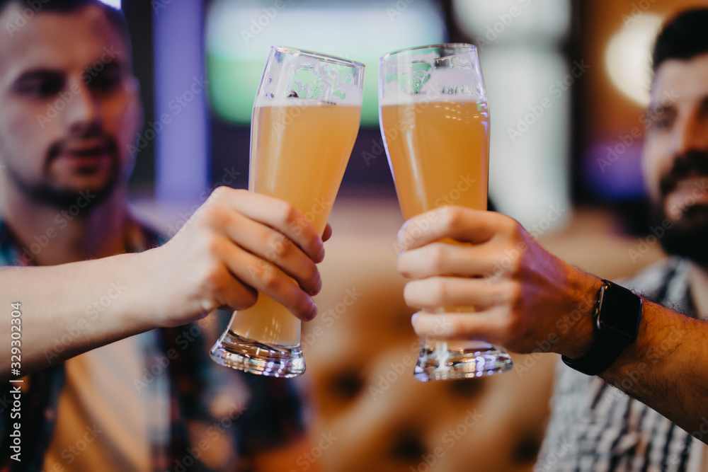 Close up of hands of two friends toasting with glasses of light beer at the pub.