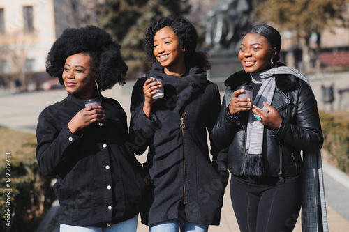 three stylish african american girls drinking coffee on the street and having fun
