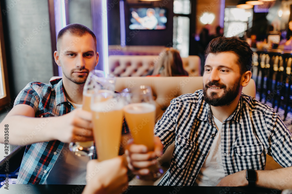 Old friends meeting. Three cheerful young men drinking beer in pub