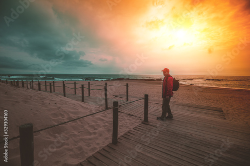 Silhouette of man on the beach goes to the sea during magical dramatic sunset. Man walking on the wooden walkway