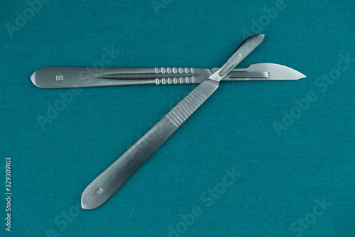 Surgical instrument, stainless steel scalpel handle number 3 with blade number 10 and scalpel handle number 4 with blade number 24 on surgical green drape fabric.