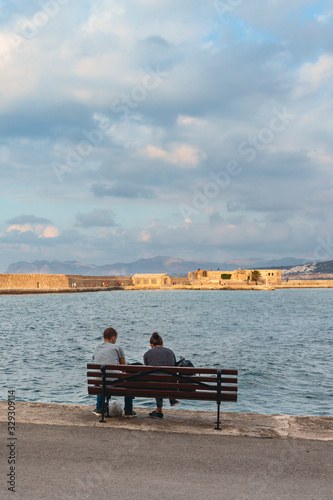 Wallpaper Mural young couple in love sitting on a bench by the sea on the waterfront of the Greek city of Chania. Torontodigital.ca