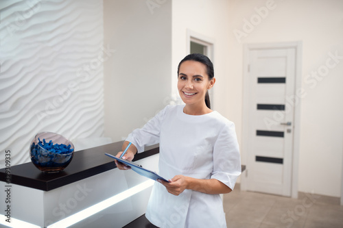 Smiling dark-eyed receptionist of beauty clinic feeling cheerful