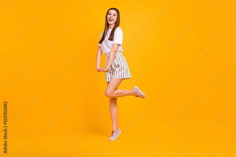 Full size profile photo of funny lady walking down street enjoy sunny day flirty mood wear casual white t-shirt striped shorts shoes isolated vibrant yellow color background