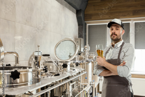 Professional brewer on his own craft alcohol production. Specialist  man wearing in workwear testing  trying product on its taste  color and smell. Concept of open business  eco product  craft brewery