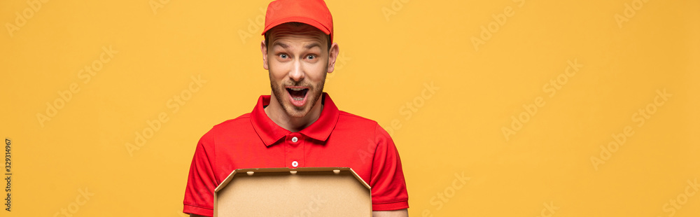 shocked delivery man in red uniform holding pizza box isolated on yellow, panoramic shot shocked delivery man in red uniform holding pizza box isolated on yellow, panoramic shot