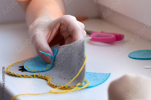 A girl sews an owl toy from felt. Scissors, thread, felt sheets on a table. Cute stuffed toy is made manually. Easy sewing project for kids