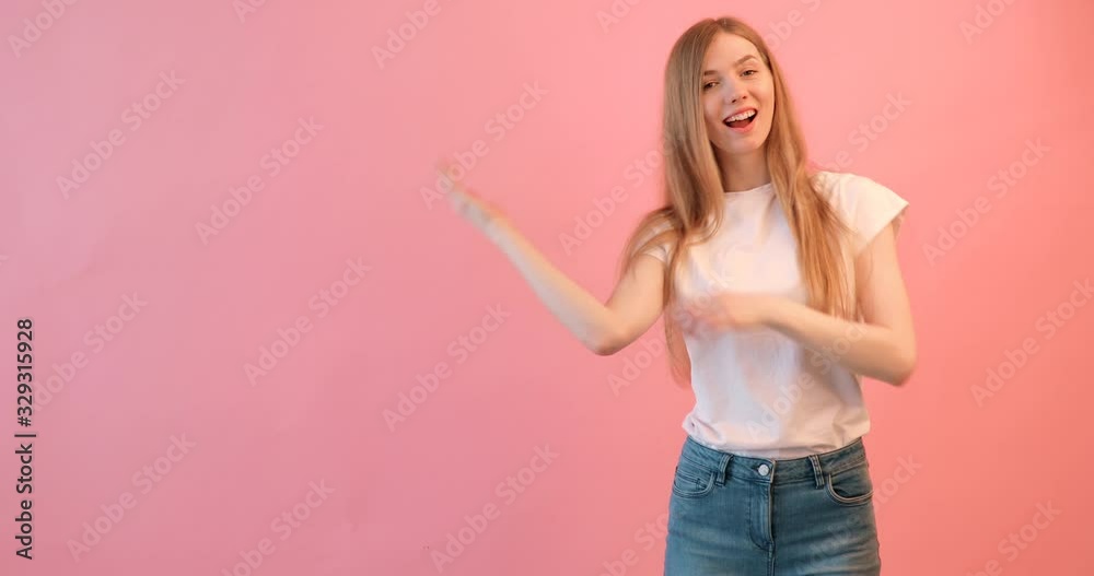 Portrait of a cheerful girl in a white t-shirt pointing a finger at an empty space on an empty background, on a pink background Portrait of a cheerful girl in a white t-shirt pointing a finger at an empty space on an empty background, on a pink background