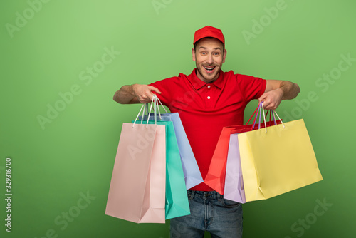 happy delivery man in red uniform holding shopping bags on green