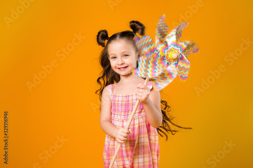 little girl smiling holding a children's windmill on a yellow background of isolate